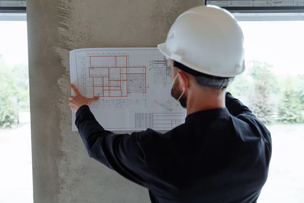 Profesional de espaldas revisando planos durante una visita a un inmueble en obra